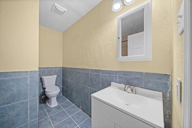 bathroom with tile walls, tile patterned flooring, vanity, toilet, and a textured ceiling