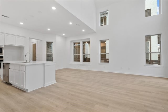 kitchen with white cabinetry, an island with sink, sink, and light hardwood / wood-style floors