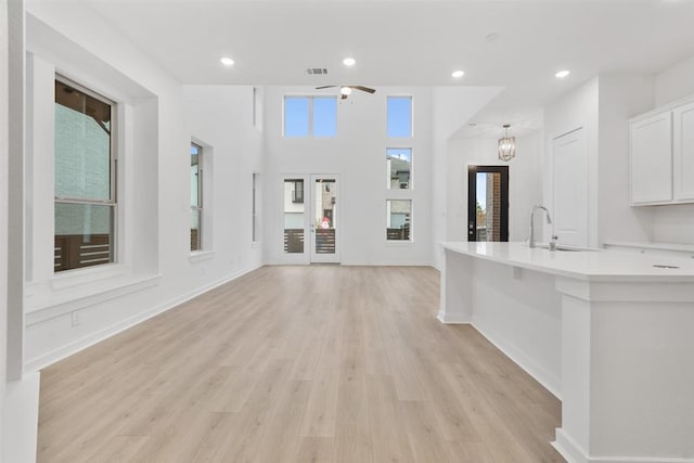 unfurnished living room featuring ceiling fan with notable chandelier, sink, and light wood-type flooring