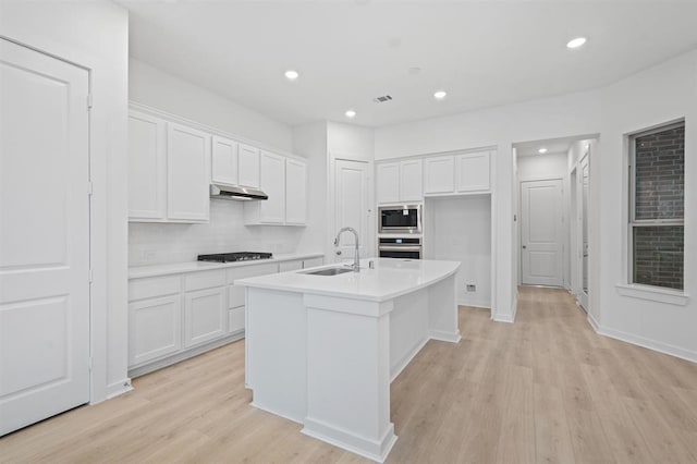 kitchen with sink, white cabinetry, a kitchen island with sink, stainless steel appliances, and light wood-type flooring