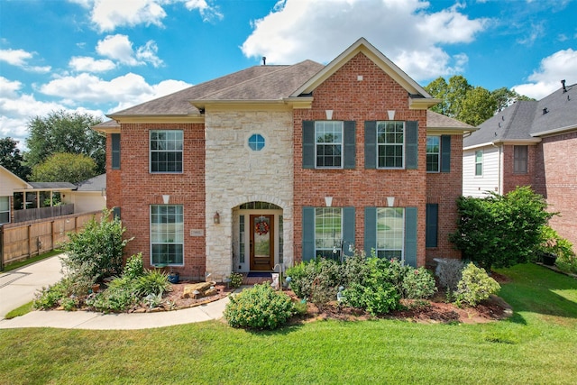 view of front facade featuring stone siding, brick siding, a front lawn, and fence