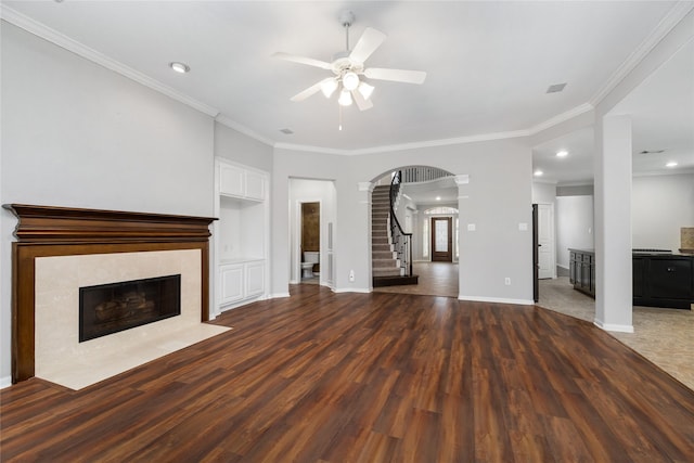 unfurnished living room featuring wood finished floors, stairway, a fireplace, and crown molding