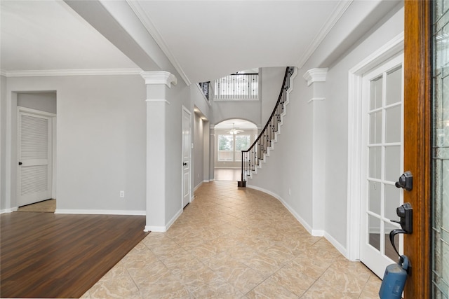 foyer with decorative columns, arched walkways, crown molding, and stairway