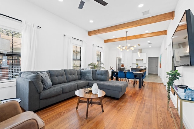 living room with ceiling fan with notable chandelier, beamed ceiling, light wood-type flooring, and a healthy amount of sunlight