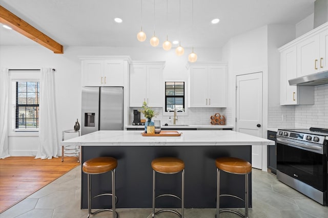 kitchen featuring white cabinetry, stainless steel appliances, a kitchen island, sink, and light stone counters