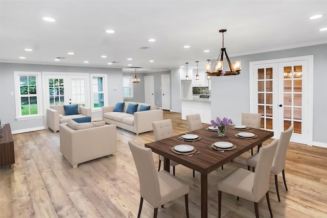 dining space with crown molding, an inviting chandelier, light wood-type flooring, and french doors