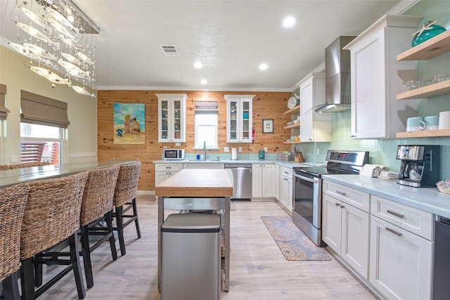 kitchen with a kitchen island, appliances with stainless steel finishes, white cabinets, and wall chimney exhaust hood