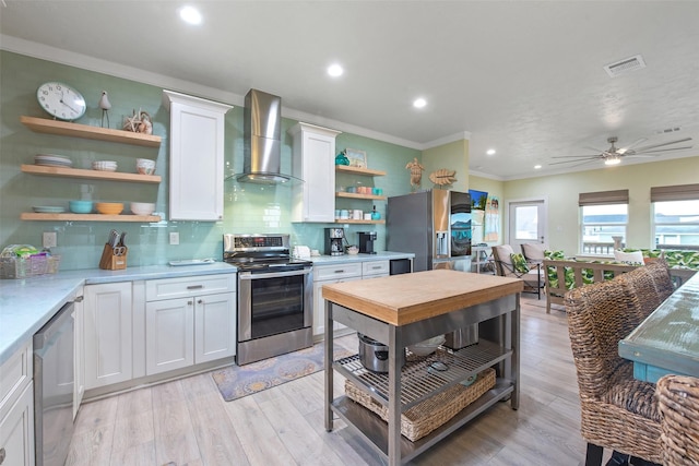 kitchen with wall chimney range hood, appliances with stainless steel finishes, white cabinetry, light hardwood / wood-style floors, and decorative backsplash