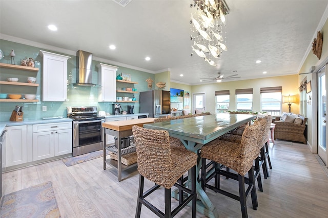 kitchen with a breakfast bar area, appliances with stainless steel finishes, white cabinetry, a center island, and wall chimney exhaust hood