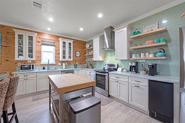 kitchen featuring sink, white cabinetry, stainless steel appliances, ornamental molding, and wall chimney exhaust hood