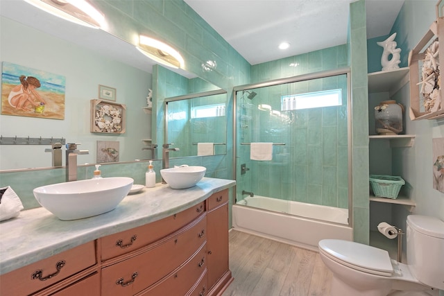 full bathroom with vanity, hardwood / wood-style floors, bath / shower combo with glass door, and toilet