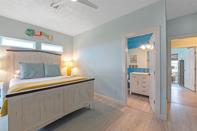 bedroom with ceiling fan, ensuite bathroom, light hardwood / wood-style flooring, and a textured ceiling