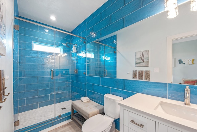 bathroom with a shower with shower door, tasteful backsplash, tile walls, vanity, and toilet