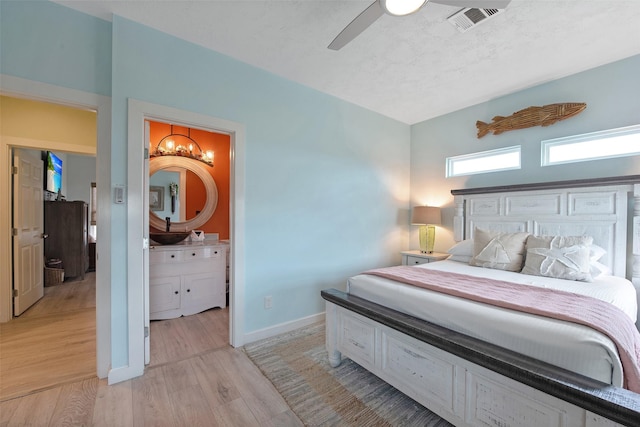 bedroom featuring connected bathroom, ceiling fan with notable chandelier, and light wood-type flooring