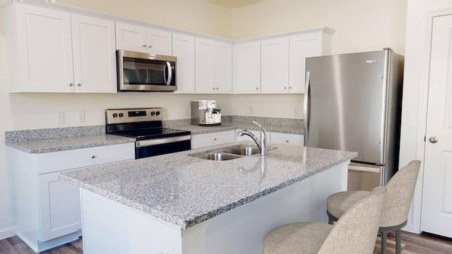 kitchen with sink, white cabinetry, a kitchen island with sink, stainless steel appliances, and a kitchen bar