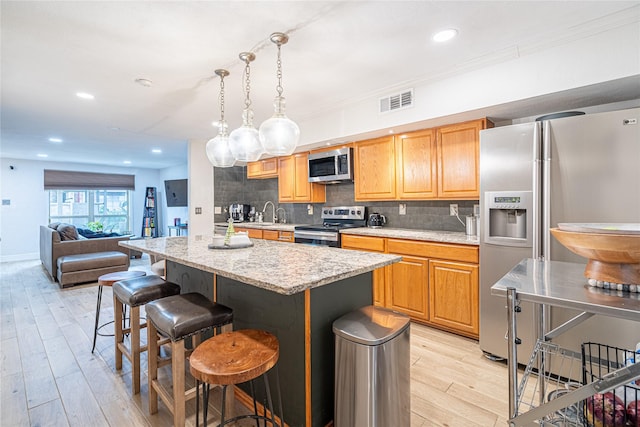 kitchen with a kitchen bar, hanging light fixtures, a center island, light hardwood / wood-style floors, and stainless steel appliances