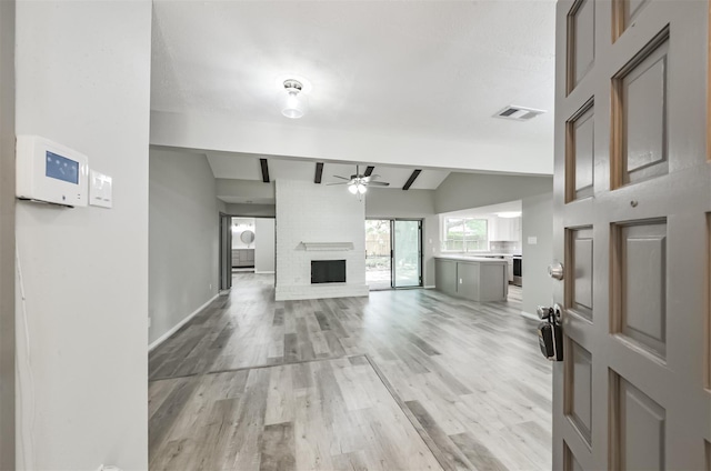 unfurnished living room with ceiling fan, a fireplace, light hardwood / wood-style flooring, and vaulted ceiling with beams