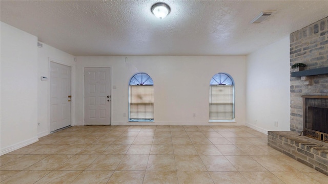 unfurnished living room with light tile patterned flooring, a brick fireplace, and a textured ceiling