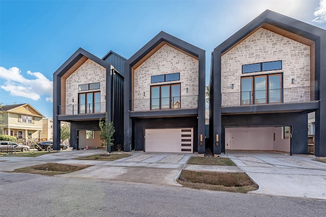 contemporary home with a garage, concrete driveway, brick siding, and stone siding