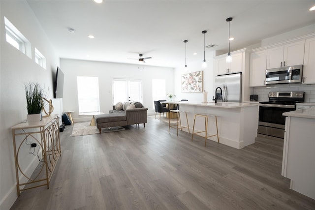 kitchen featuring hardwood / wood-style flooring, a breakfast bar, white cabinetry, a kitchen island with sink, and stainless steel appliances