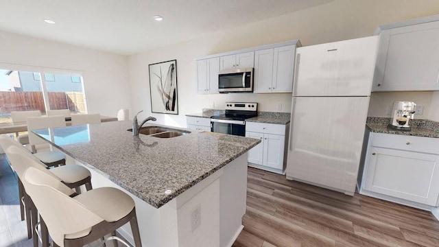 kitchen featuring sink, appliances with stainless steel finishes, an island with sink, white cabinets, and dark stone counters