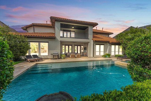 back of property with a balcony, an outdoor hangout area, stucco siding, an outdoor pool, and a patio area