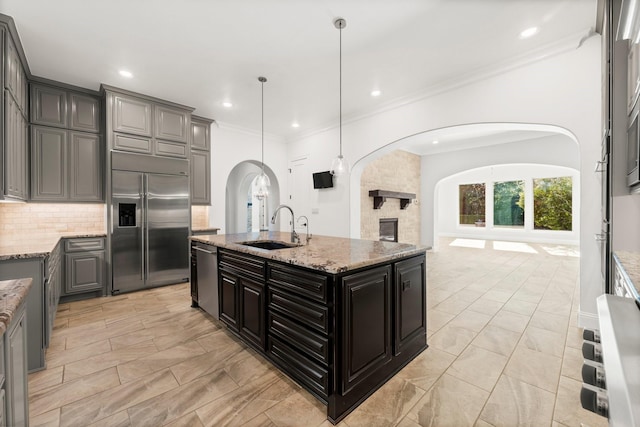 kitchen featuring arched walkways, a sink, open floor plan, appliances with stainless steel finishes, and decorative backsplash