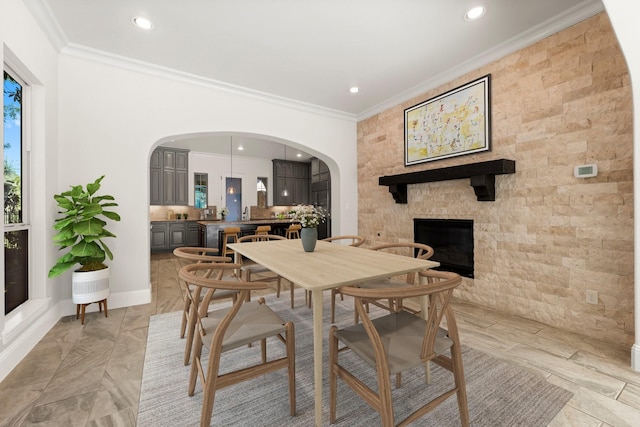 dining space with ornamental molding, arched walkways, a fireplace, and recessed lighting