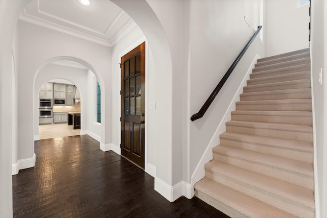 foyer with ornamental molding, arched walkways, dark wood finished floors, and baseboards