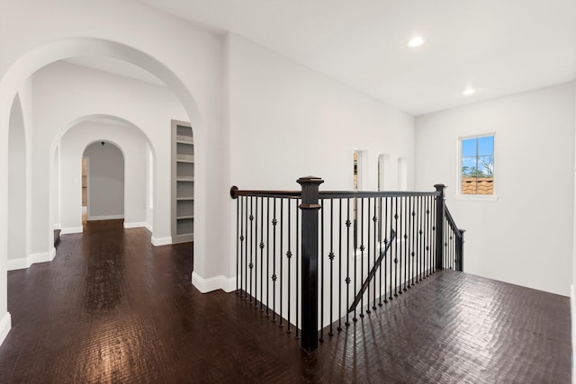 corridor with baseboards, arched walkways, wood finished floors, an upstairs landing, and recessed lighting