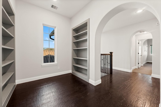 empty room featuring built in shelves, visible vents, baseboards, and wood finished floors