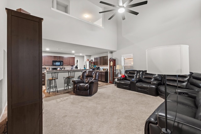 living room featuring ceiling fan, light colored carpet, and a high ceiling