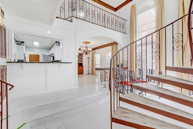 staircase featuring a notable chandelier, a towering ceiling, and ornamental molding