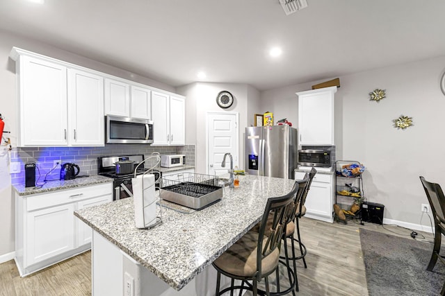 kitchen featuring white cabinetry, light stone counters, a center island with sink, stainless steel appliances, and light hardwood / wood-style floors