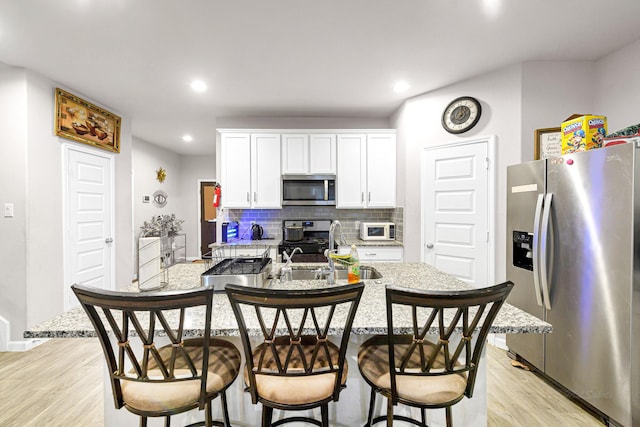 kitchen featuring appliances with stainless steel finishes, an island with sink, sink, white cabinets, and a kitchen breakfast bar