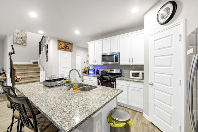 kitchen featuring white cabinetry, stainless steel appliances, a kitchen island with sink, and sink