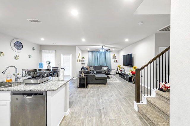 kitchen with sink, light stone counters, light wood-type flooring, stainless steel dishwasher, and white cabinets