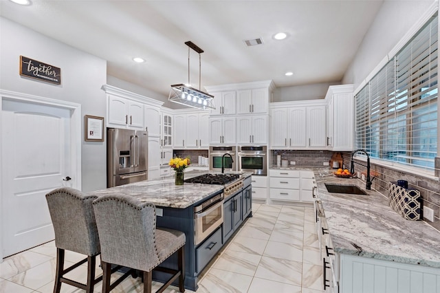 kitchen with appliances with stainless steel finishes, white cabinetry, sink, hanging light fixtures, and a center island