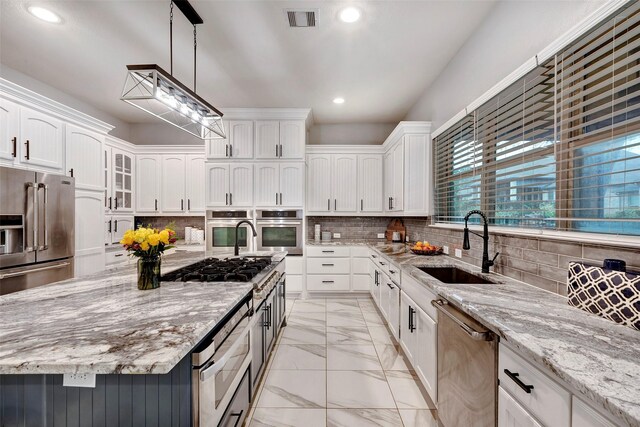 kitchen with sink, appliances with stainless steel finishes, hanging light fixtures, light stone counters, and a kitchen island