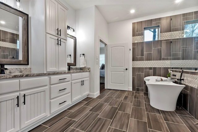 bathroom featuring vanity, a bath, and tile walls