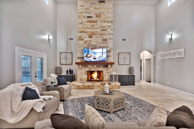 living room with a stone fireplace, french doors, and a towering ceiling