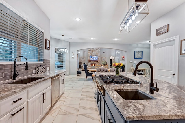 kitchen with sink, hanging light fixtures, light stone countertops, and an island with sink