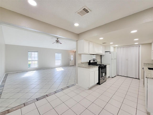 kitchen featuring white cabinetry, light stone counters, light tile patterned flooring, gas range, and white fridge