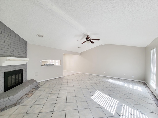 unfurnished living room with ceiling fan, lofted ceiling with beams, a textured ceiling, light tile patterned flooring, and a brick fireplace