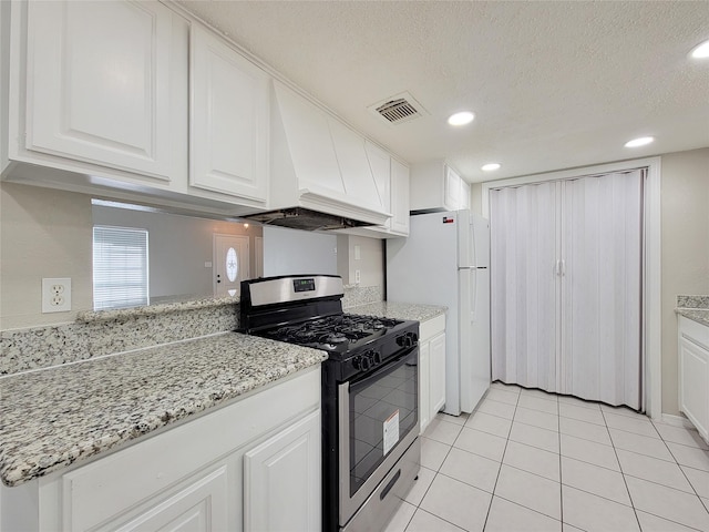 kitchen with light tile patterned floors, white cabinetry, stainless steel gas range oven, light stone countertops, and custom exhaust hood