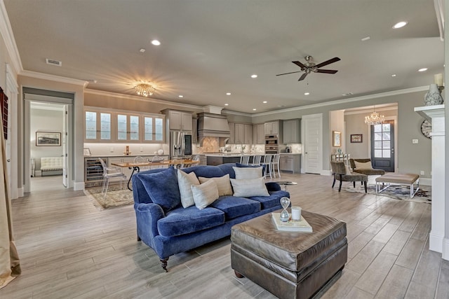 living room with crown molding, wine cooler, ceiling fan with notable chandelier, and light wood-type flooring