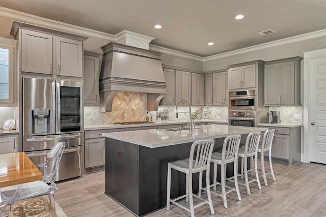 kitchen featuring appliances with stainless steel finishes, an island with sink, sink, backsplash, and custom exhaust hood