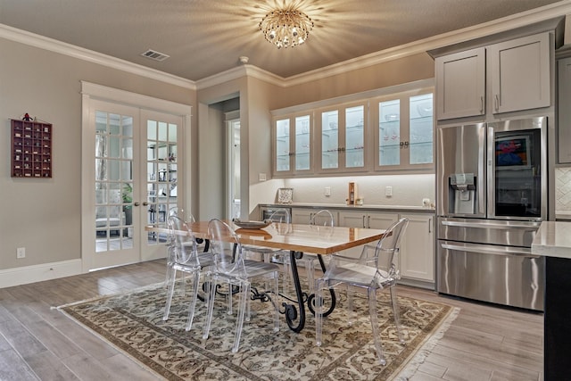 dining space with light wood-type flooring, crown molding, a textured ceiling, an inviting chandelier, and french doors