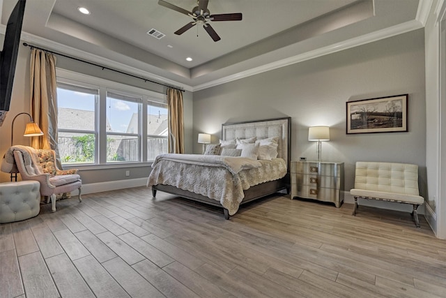 bedroom with ceiling fan, a tray ceiling, and light wood-type flooring