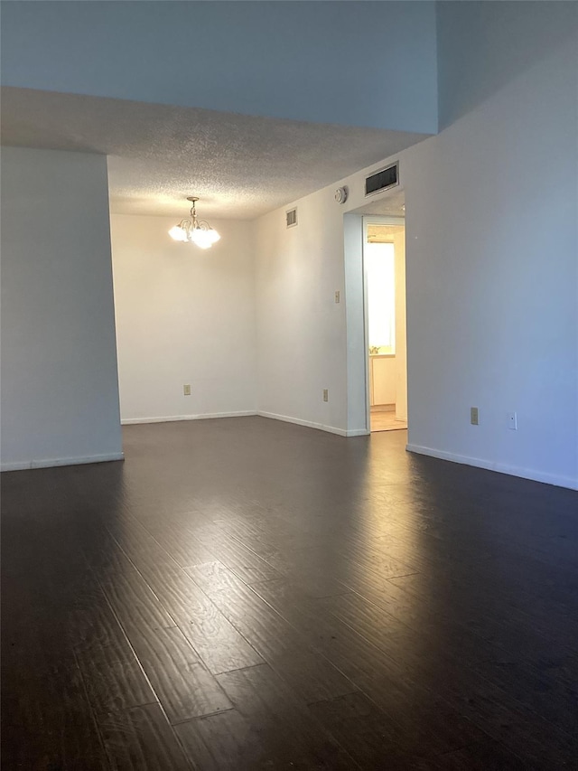 unfurnished room with an inviting chandelier, dark wood-type flooring, and a textured ceiling